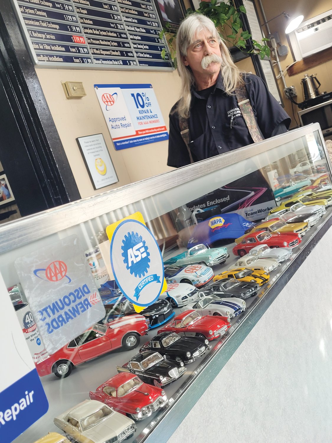 TINY CARS: Dave Carrara stands over a small glass display case in the lobby of Carrara’s Auto Clinic at 1225 Atwood Ave. in Johnston. He’s getting ready to retire and shared some memories from the early days of the business.